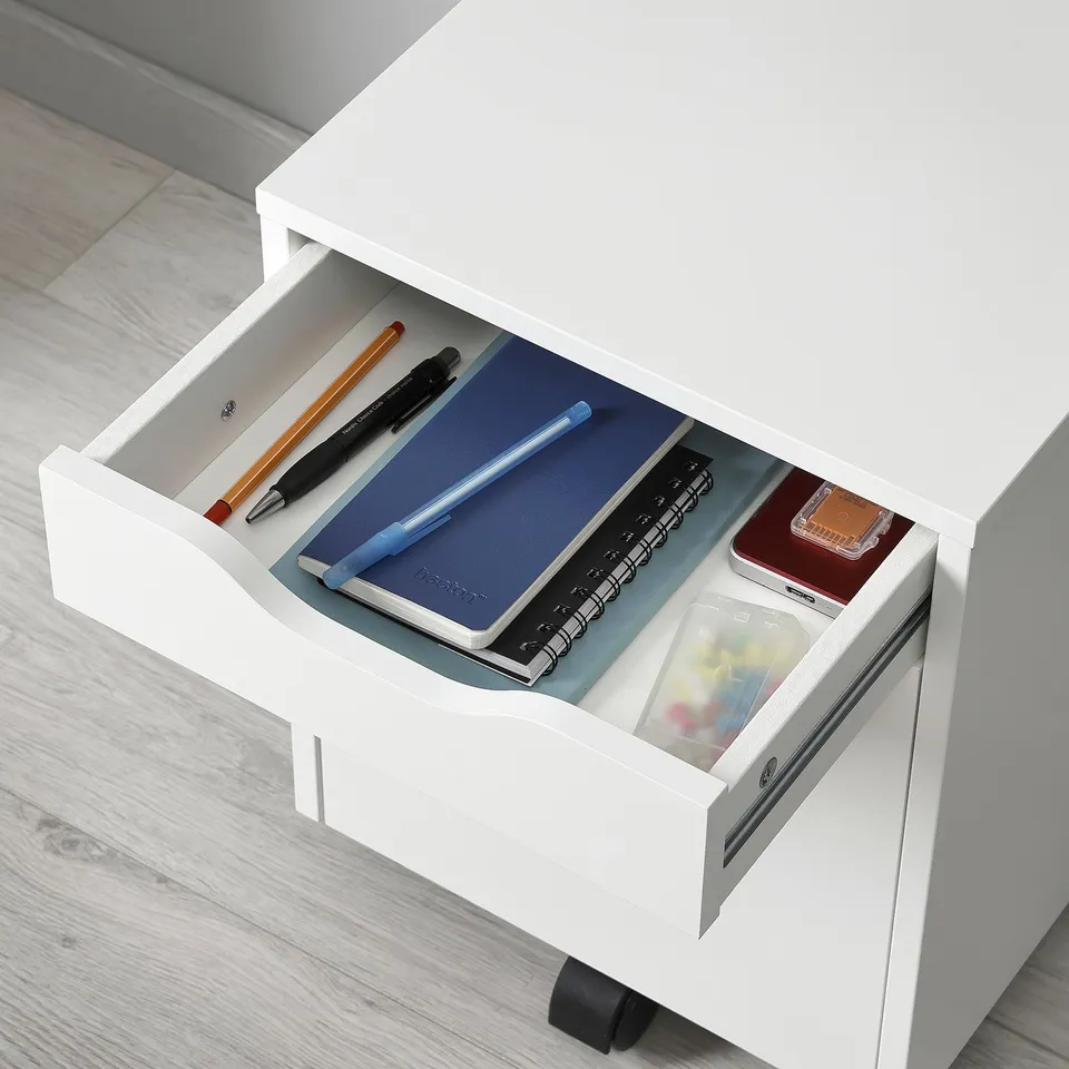 Open white drawer unit displaying various stationery items: pens, pencils, notepad, ruler, and small containers. Ideal for desk organisation.