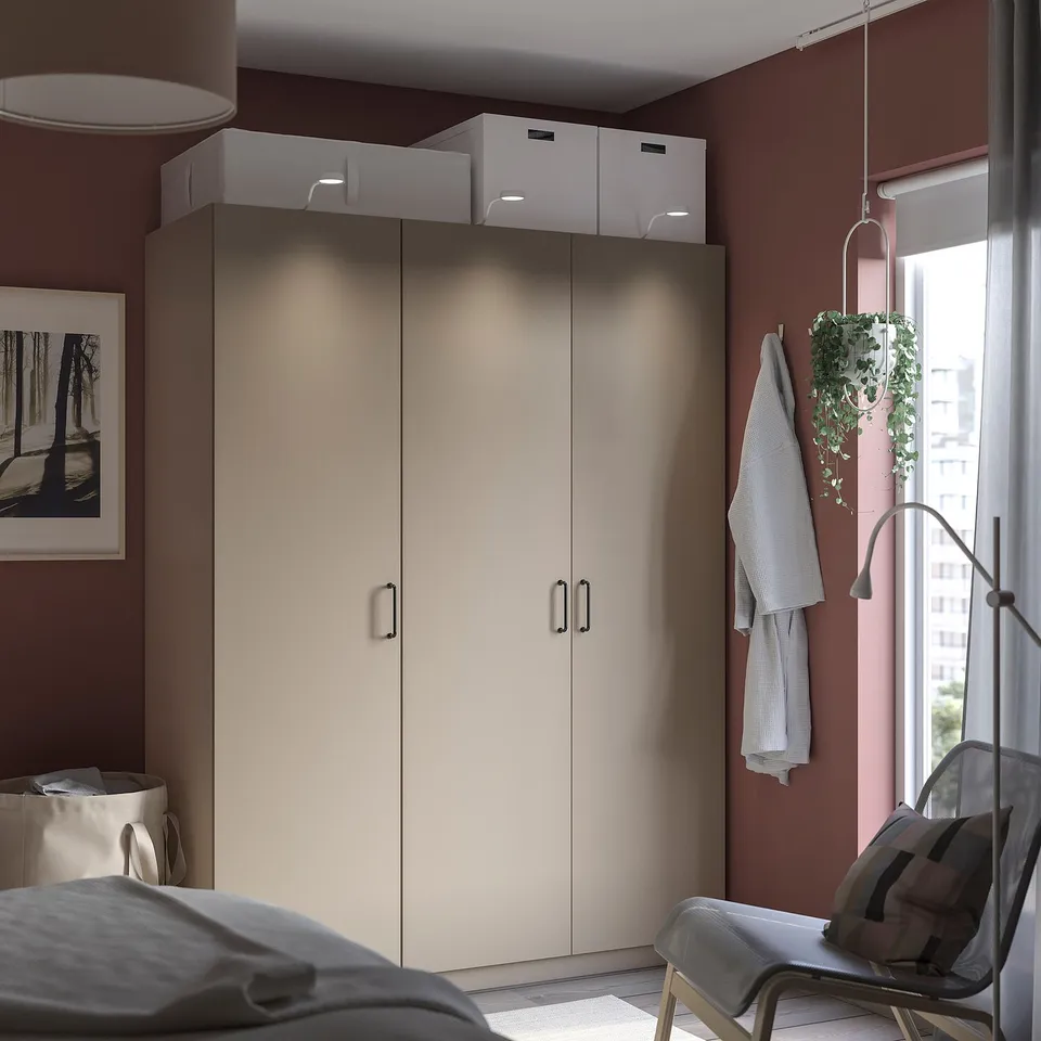 Modern bedroom with maroon walls, beige wardrobe, white chair, pictures, hanging plant, and window.