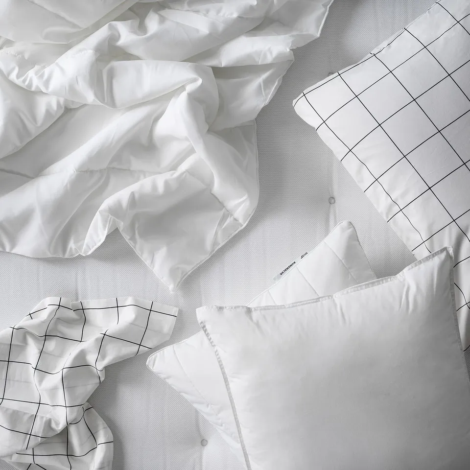 White bedding set with grid pattern pillowcases, soft fabric, recycled materials, visible folds.