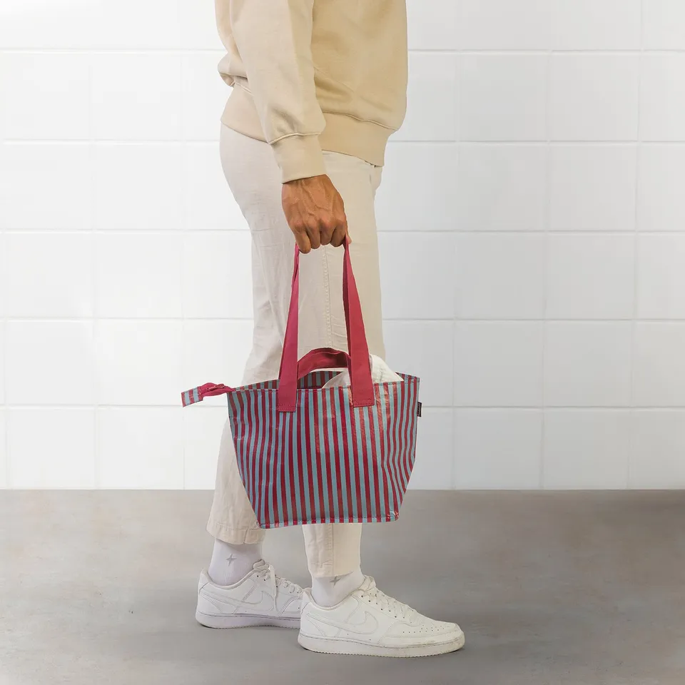 Person holding red-striped tote bag with long straps.