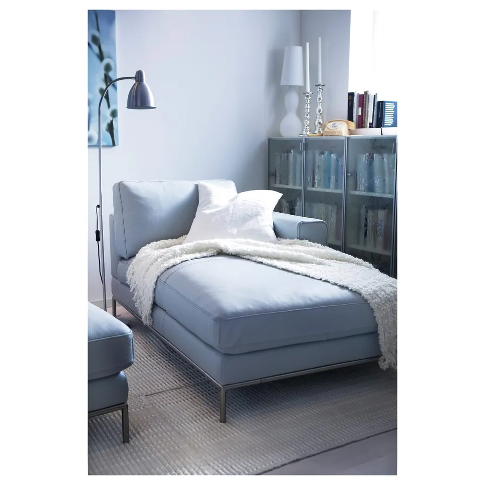 Light blue LERSTA sofa with white blanket, glass bookshelf behind, floor lamp to left, books and decor on shelf, cosy modern living space.