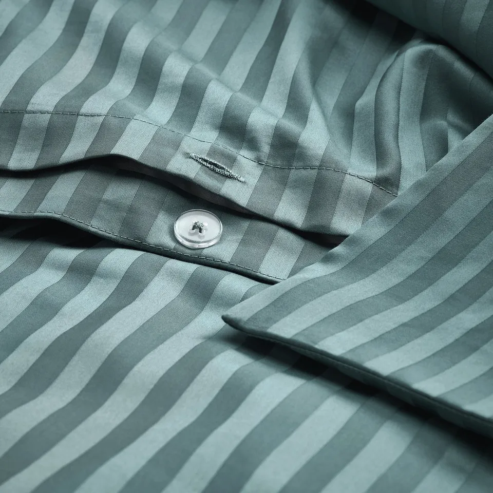 A close-up of a striped green duvet cover with a button closure. The pattern wavy stripes, and a small label is visible on the folded fabric.