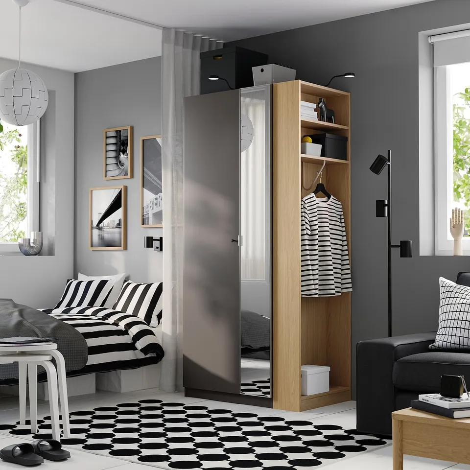 Modern bedroom: PAX wardrobe, bed with boho pillows, geometric rug, grey couch, two windows.