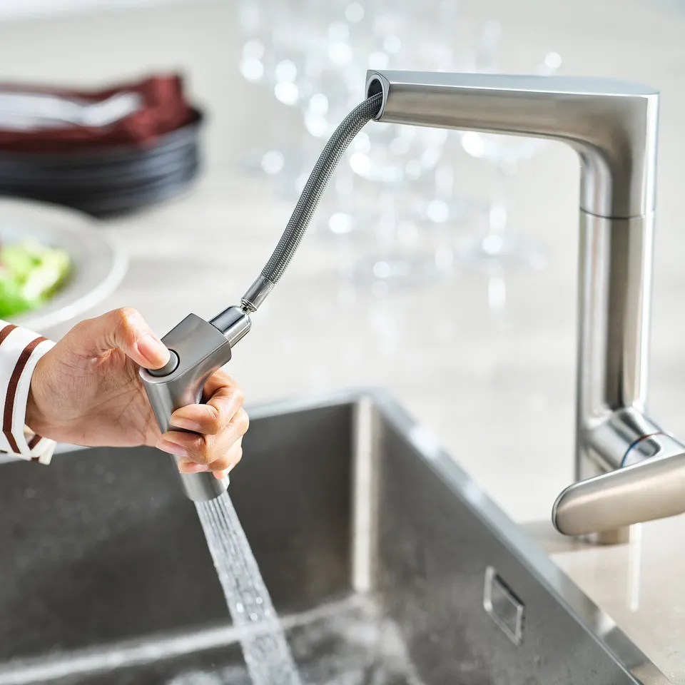 Hand using kitchen tap with spray head.