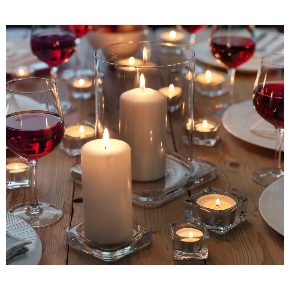 Wooden table set with white candles in clear glass holders, red wine glasses, and plates. Cosy, warm ambiance.