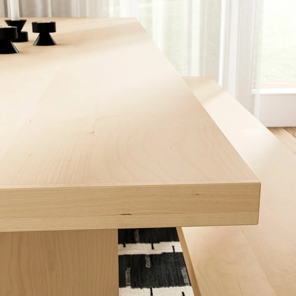 Modern light wood dining table with sleek surface, adjustable feet, and black geometric rug underneath, shown indoors.