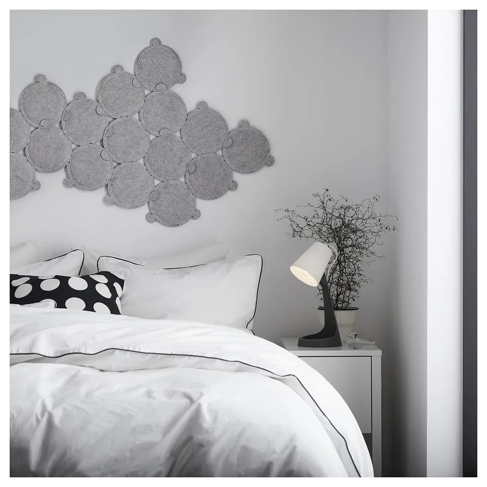Bedroom with white bedding, black-and-white polka dot pillow, lit lamp on bedside table with bare branch plant, and grey circular wall decor.