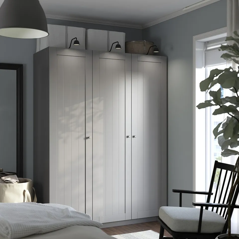 Modern bedroom with PAX wardrobe, lamp, plant, and chair.