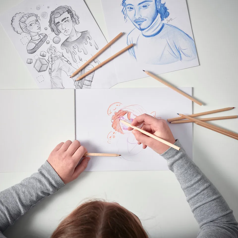 A child draws on a canvas pad with coloured pencils. Sketches include portraits and artistic designs.