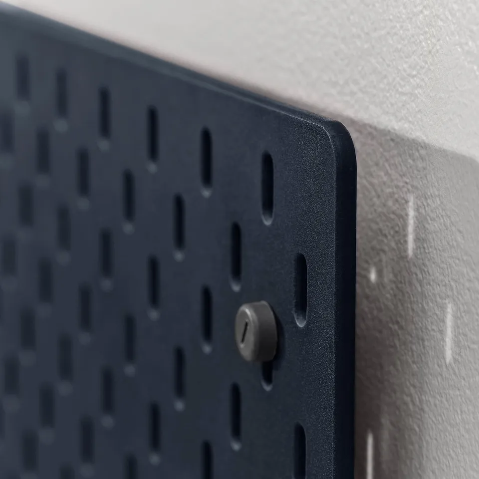 Close-up of a gray-blue SKÅDIS pegboard with a single black peg inserted, mounted on a white wall.