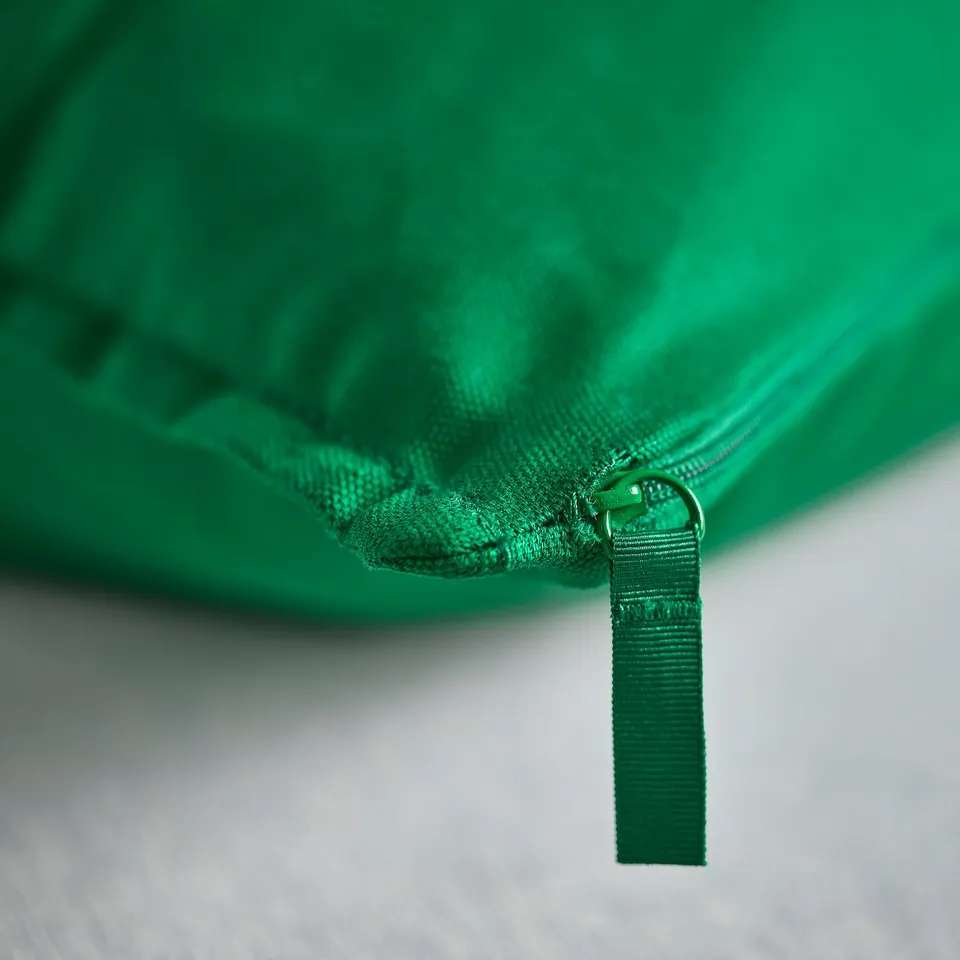 Green cushion cover with zip, attached loop, on white surface.