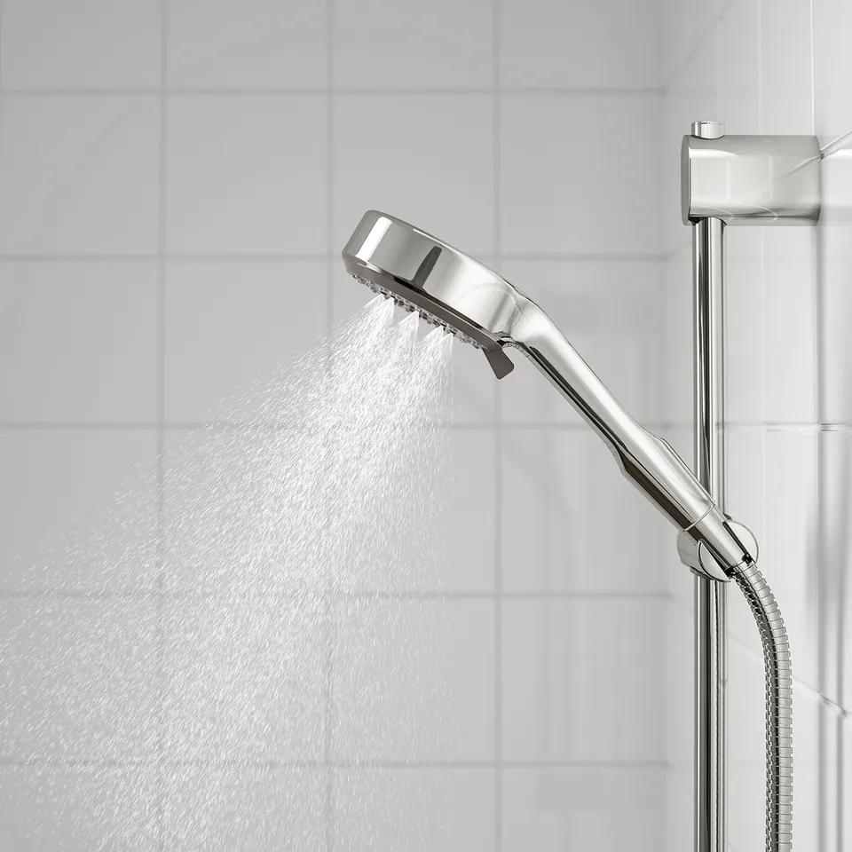 A chrome showerhead spraying water, offering full spray function, mounted on a wall with white tiles. A flexible hose is attached.