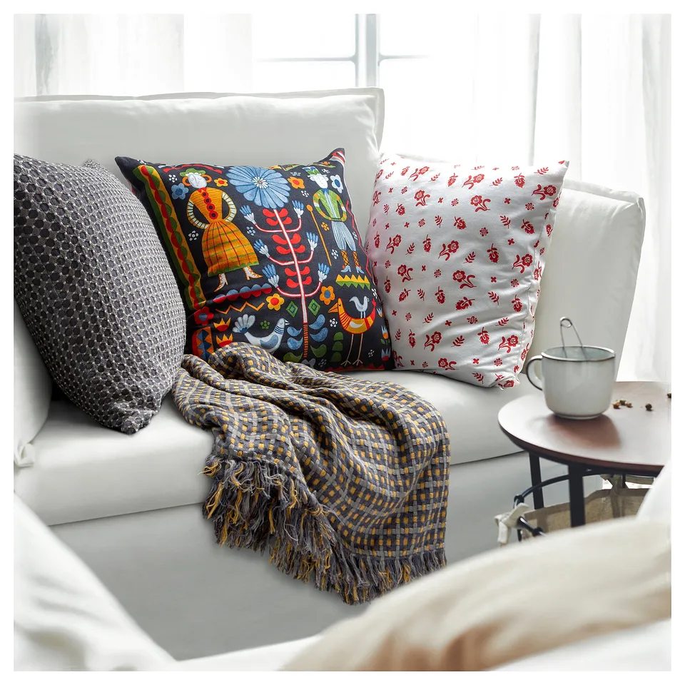 Cosy white sofa with colourful pillows and striped blanket. Floral and traditional patterns. Side table with mug and coffee beans.