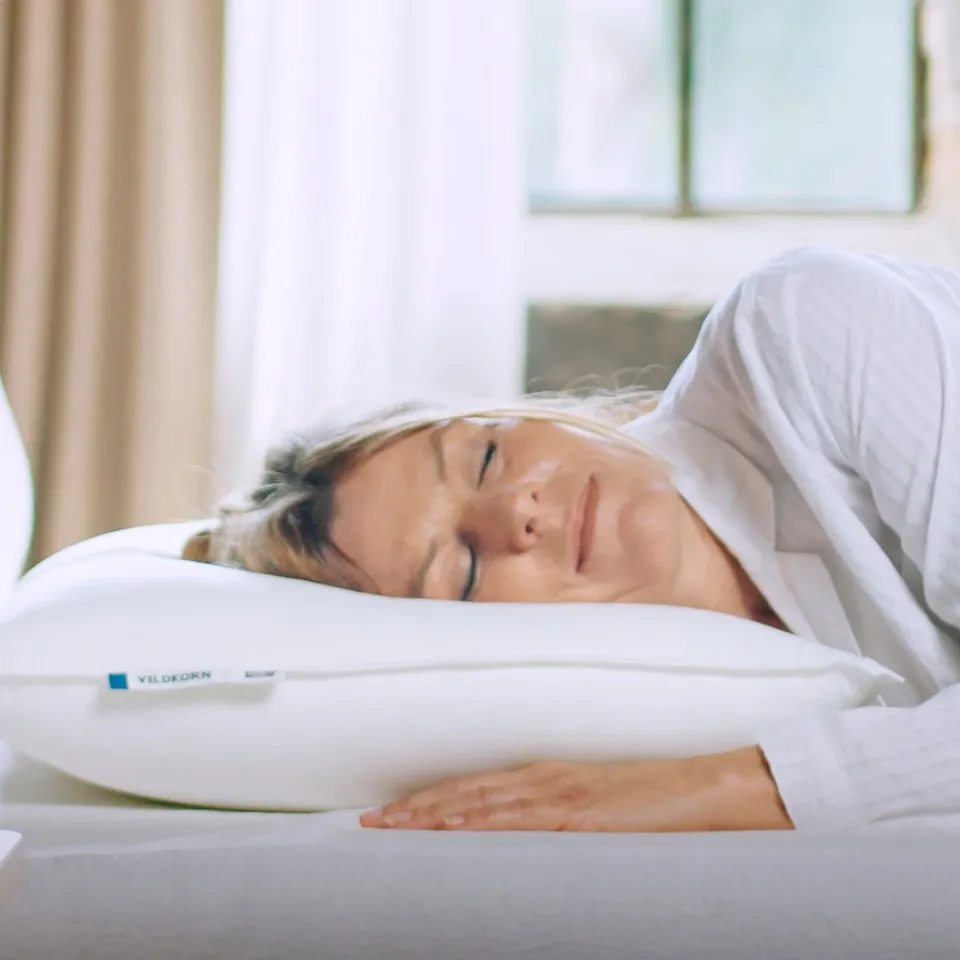 Person sleeps on plump VILDKORN pillow, green curtains.