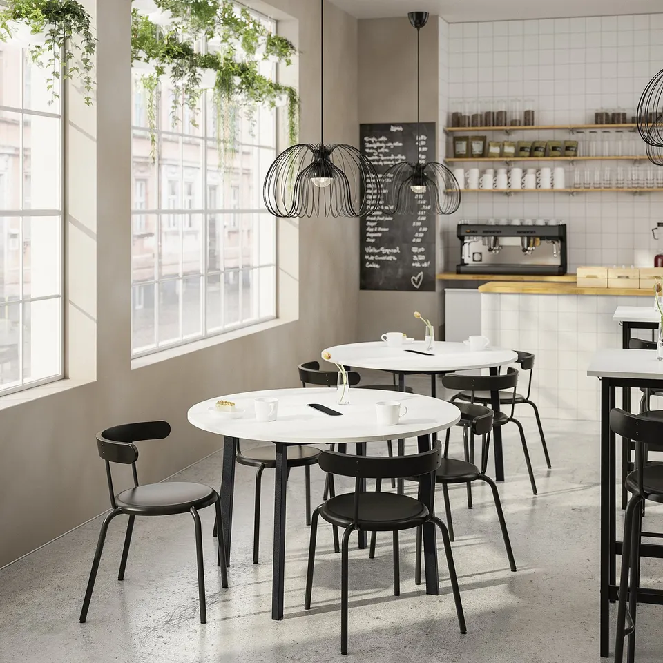 Modern cafe with round white MITTZON tables, black chairs, large window, and hanging lights.