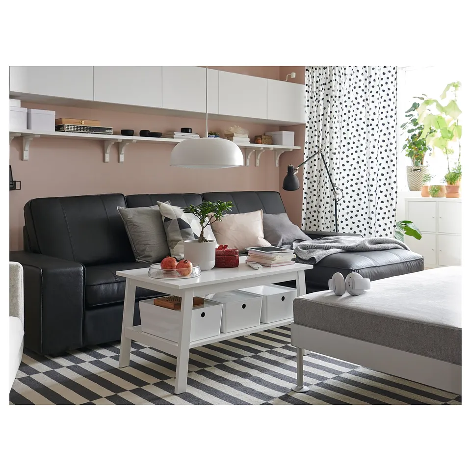Modern living room with black leather KIVIK sofa, white coffee table, striped rug, and black pendant lamp.