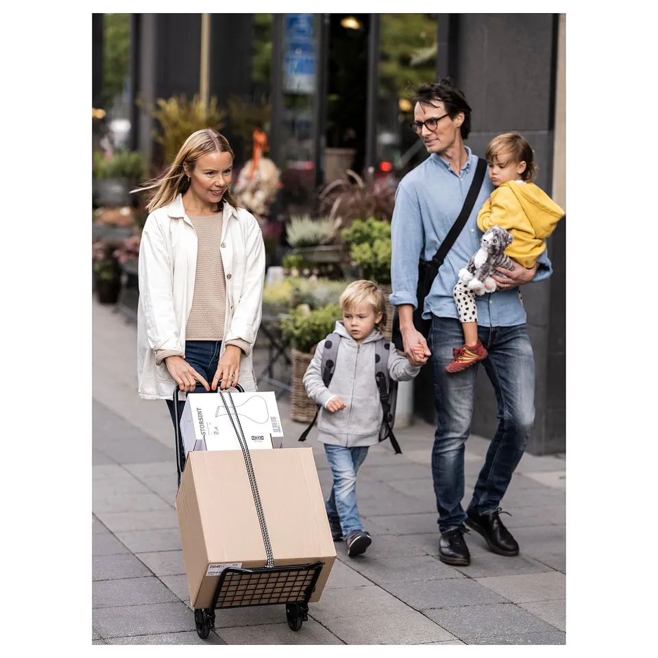 Family strolls city street. Mum with kids in tow pushes shopping trolley.