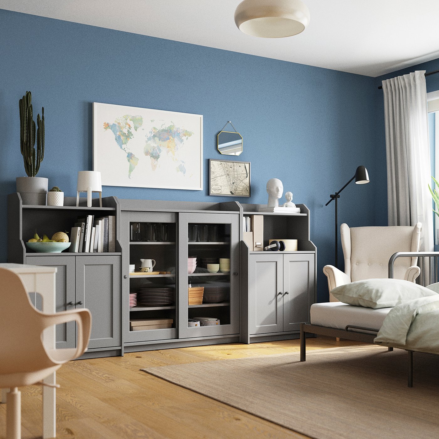 Contemporary living space with blue walls, grey HAUGA storage units, white map, cactus, and a beige chair.