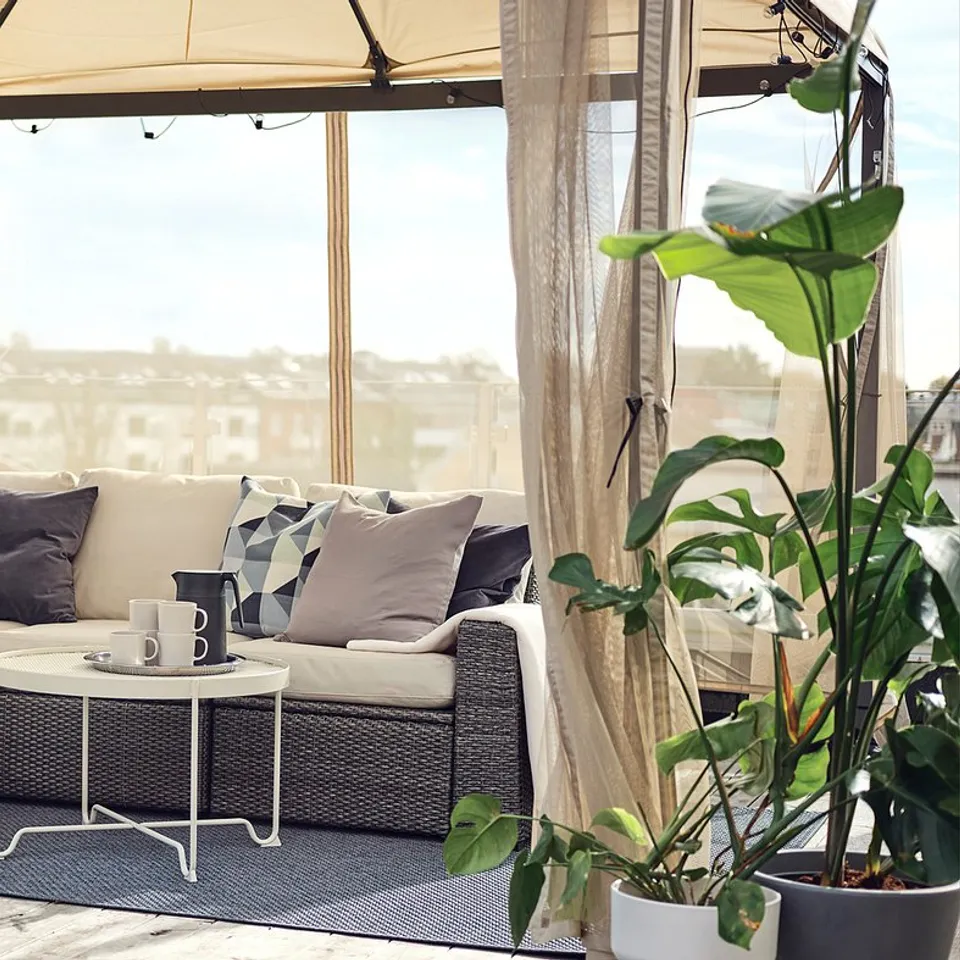 Cosy patio space with beige and cream outdoor sofa, grey cushions, and blue kids table under a beige canopy tent.