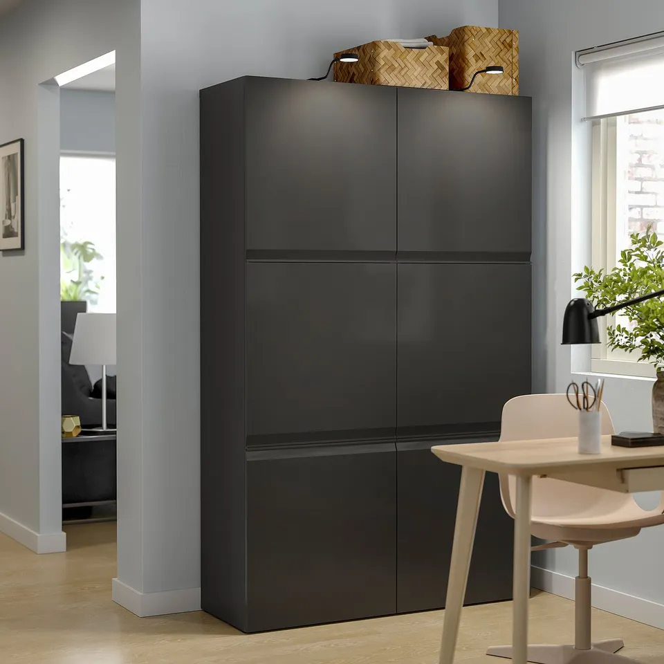 Modern living room with black BESTÅ storage unit, wooden chair, lamp, and plant.