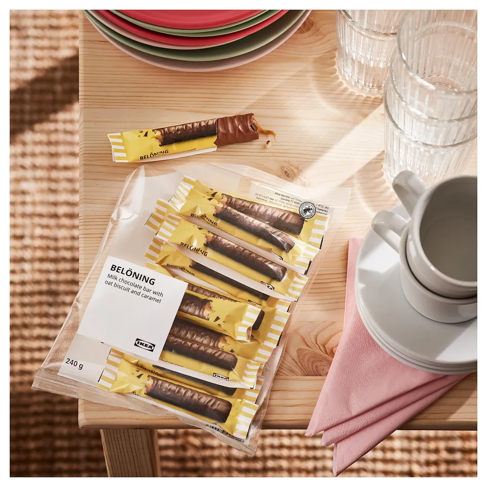 Chocolate bars labelled BELÖNING, wrapped and unwrapped, with plates and mugs on a wooden table.