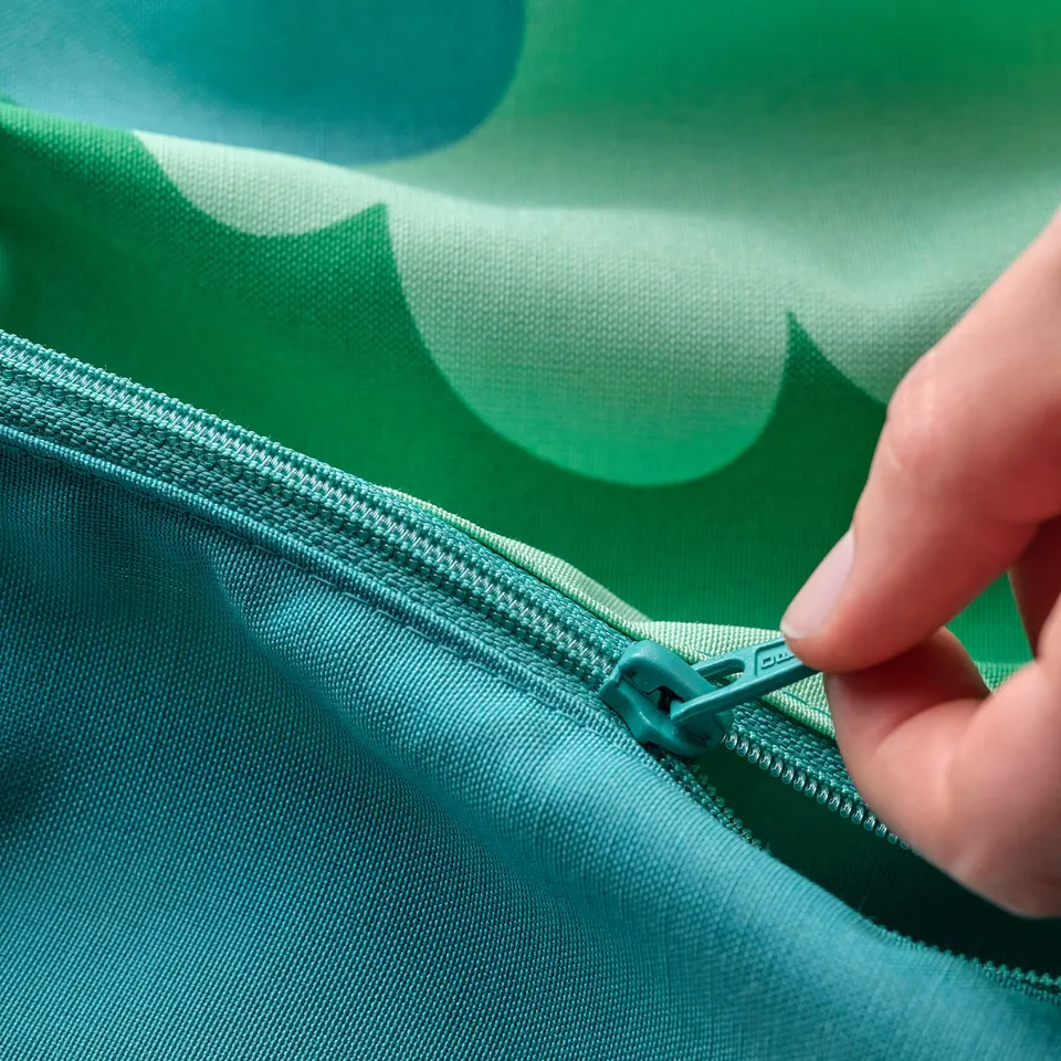 A hand zipping open a green, tree-patterned baby seat cushion.