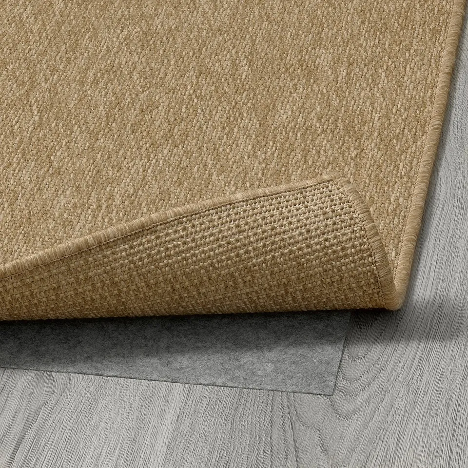 Close-up of beige flatwoven rug folded on wooden floor, showing texture and durability.