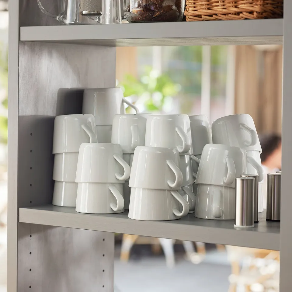 Shelf with neatly stacked white mugs, some with handles, metal canisters on right side.