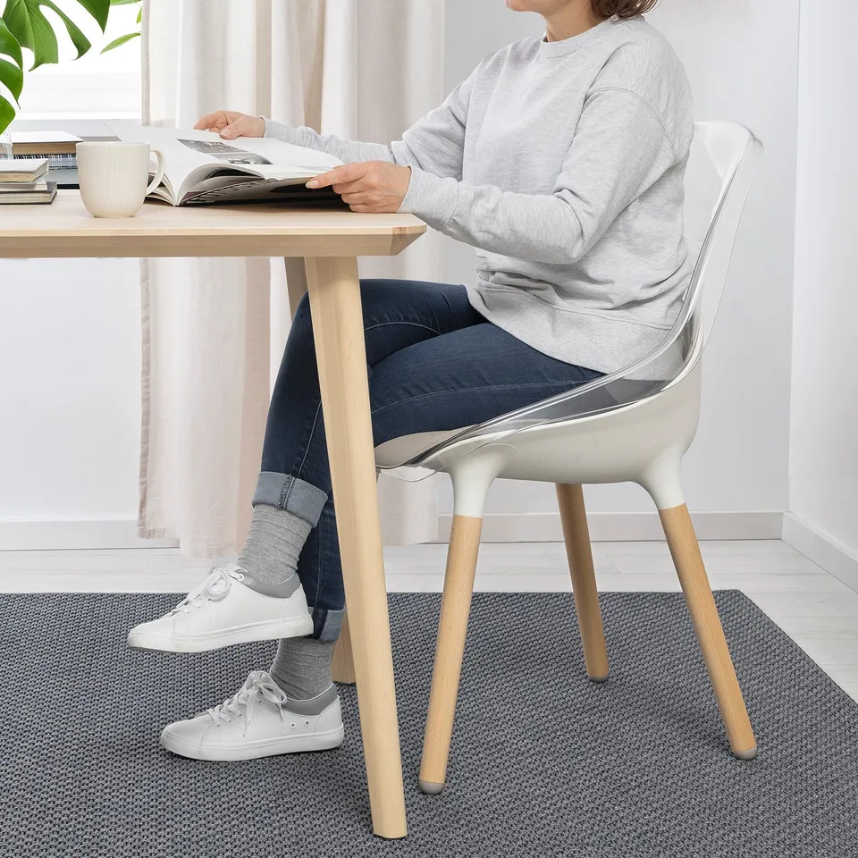 A person reads in BALTSAR chair at wooden table.
