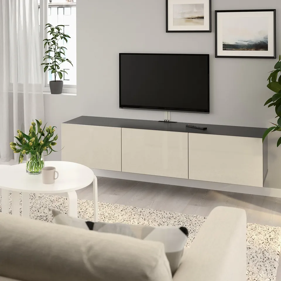 Modern living room with flat-screen tv on BESTÅ bench, storage cabinets, coffee table with flowers, and abstract paintings.