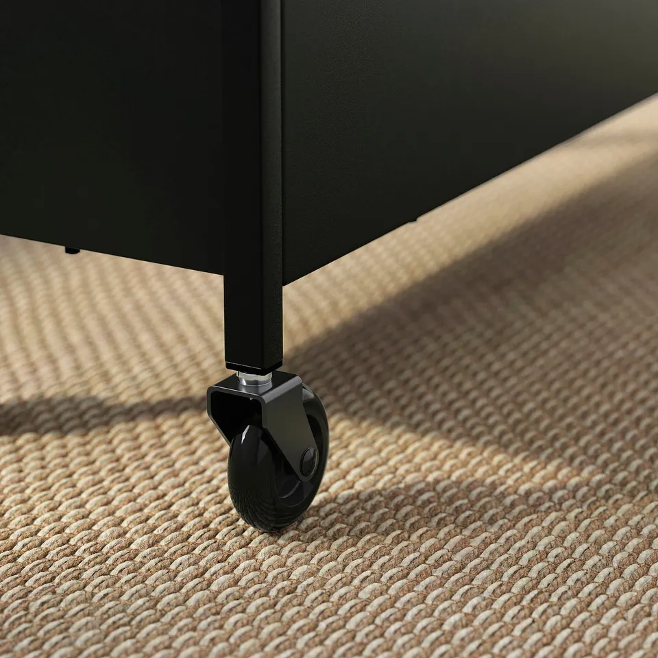 Black metal trolley with wheels on a woven rug. Sturdy and mobile, showcasing quality construction.