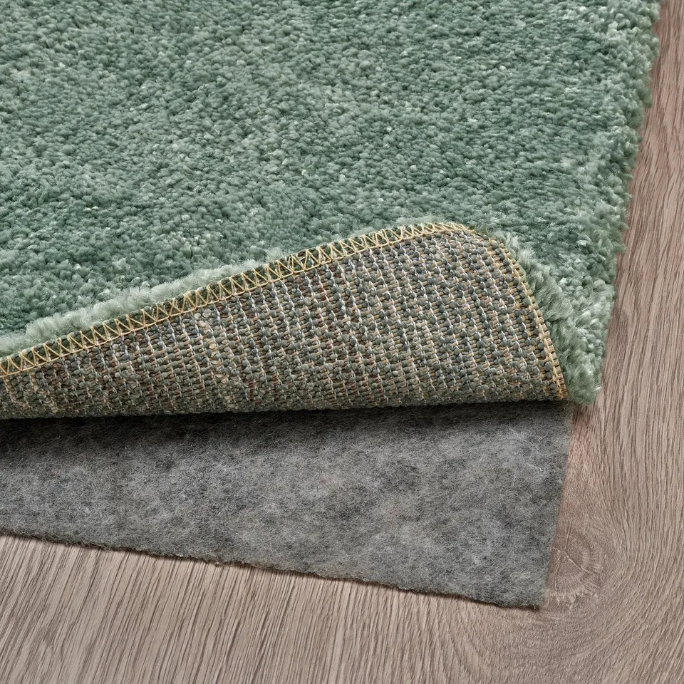 A green low-pile rug placed on a dark grey rug underlay, showcasing its anti-slip function.