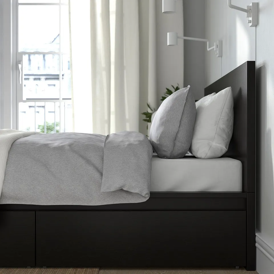 Modern bed with drawers, two large pillows, and a wall-mounted light, offering storage and comfort.