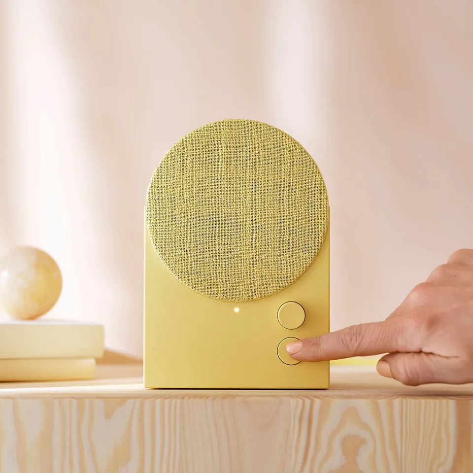 Hand presses button on golden speaker; globe on books.