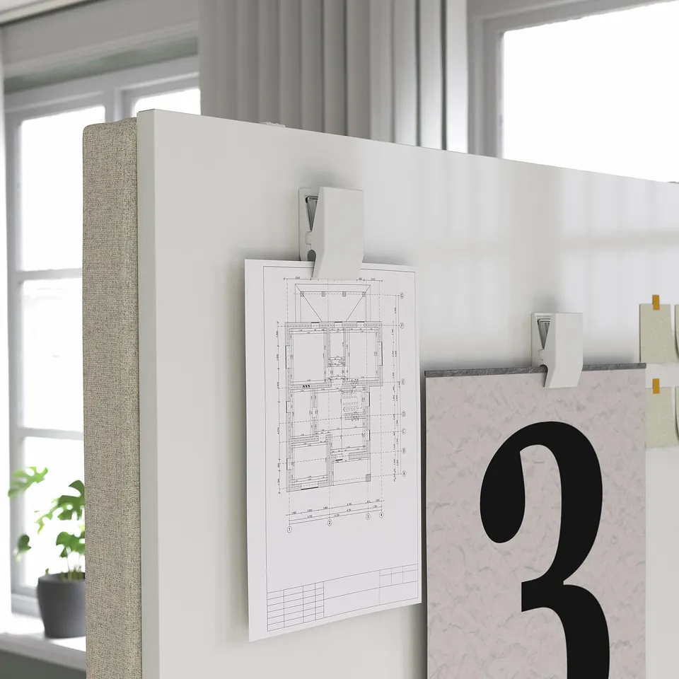 Office room divider screen with whiteboard. Clips hold paper with diagrams. Plant beside, window in background.