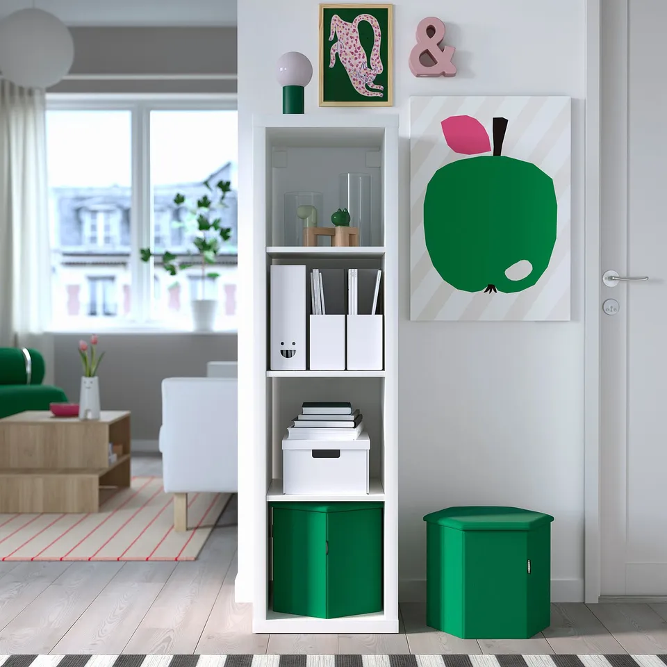 Living room with KJUGE pouffe in kallax, green chair, white sofa, apple artwork, natural light.