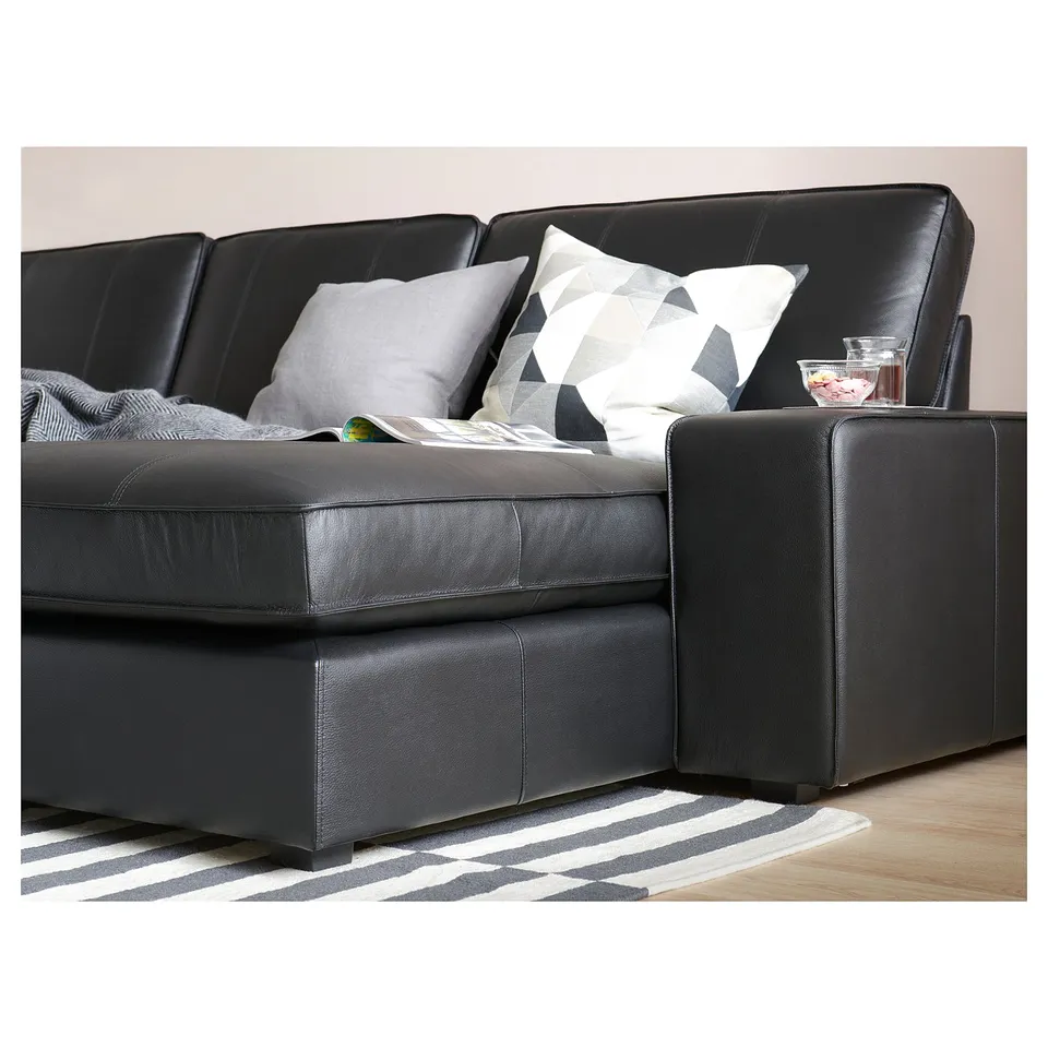 Modern black leather sectional sofa with square cushions and geometric throw pillows on a striped rug.