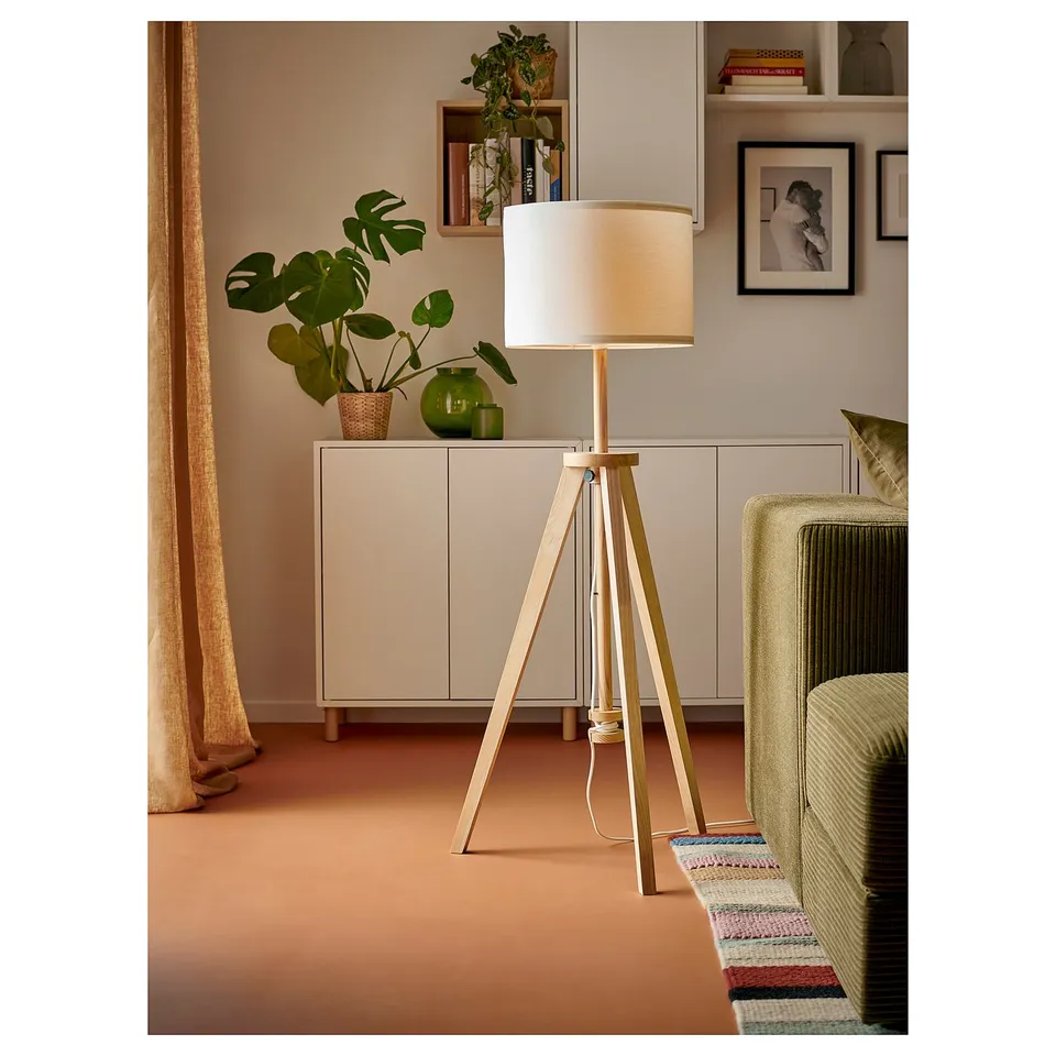 Modern living room with white LAUTERS lamp. Cylindrical shade, wooden legs. Beside cabinet with plant and decor.