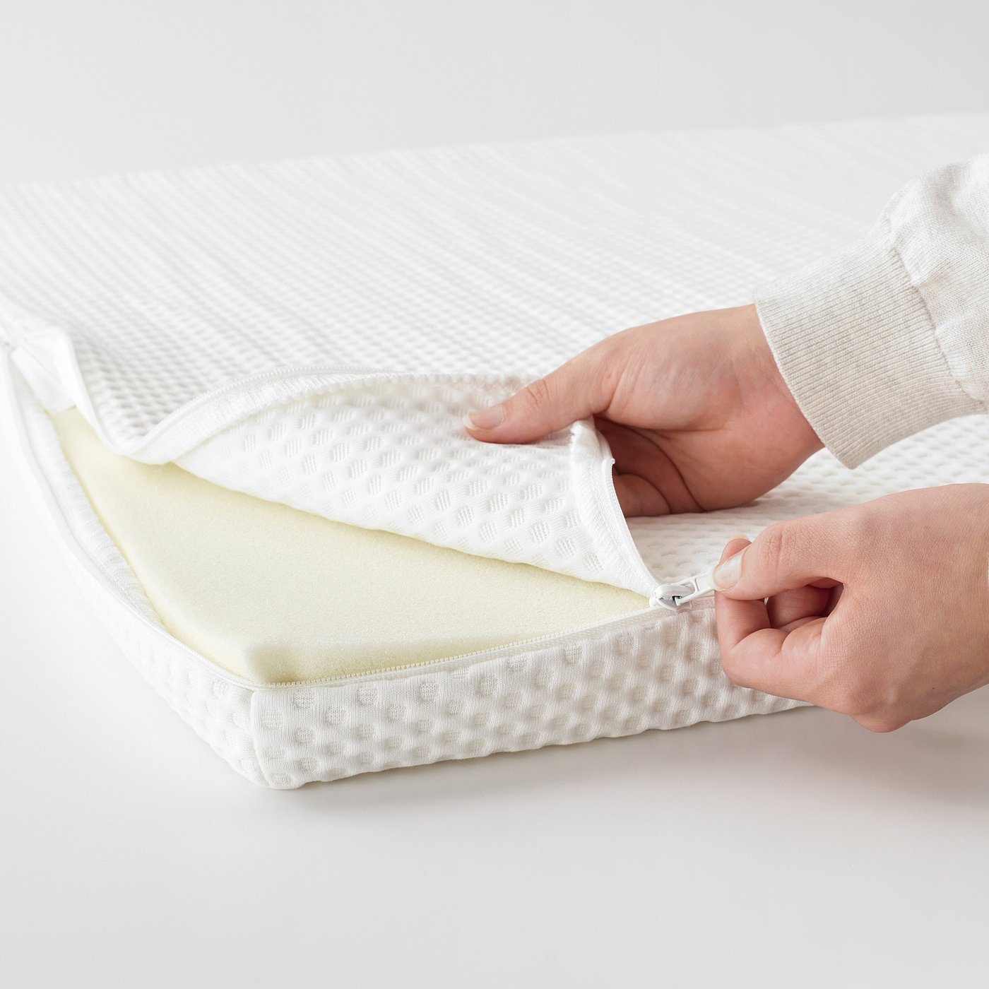 Person zips up a white, textured mattress pad, showcasing its removable cover for easy cleaning.