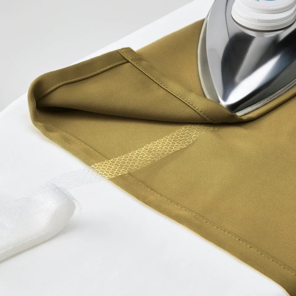 Olive-green curtain folded on white surface with an iron nearby, illustrating its texture and readiness for ironing.