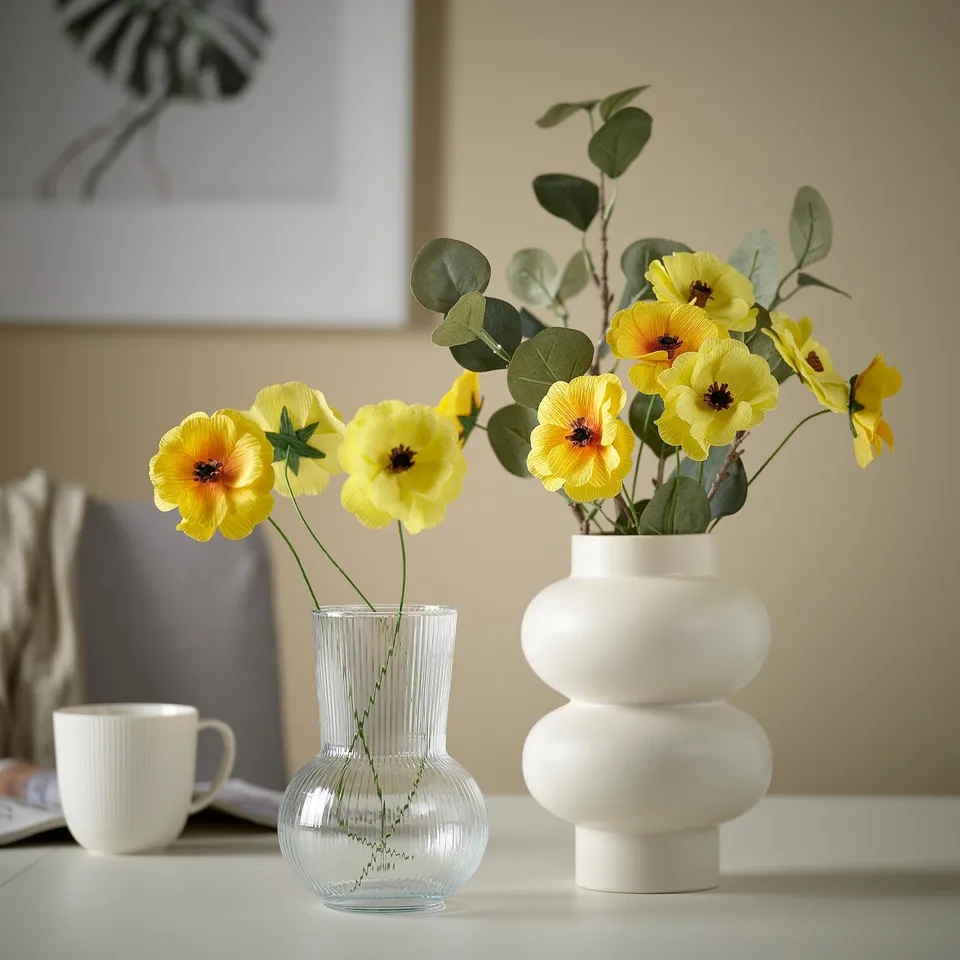 Two vases with yellow flowers. Left: clear ribbed vase. Right: large white modern vase.