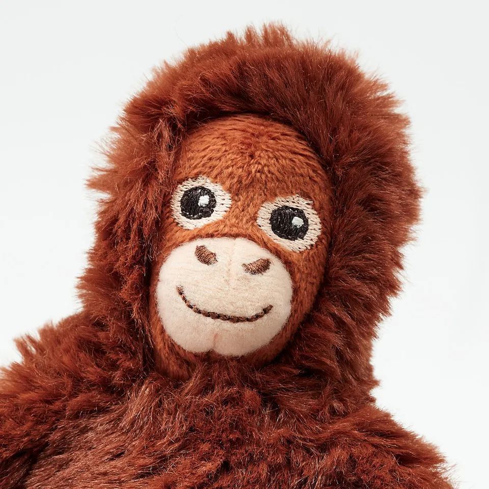 Plush orange toy monkey with embroidered smiley face, large round eyes, and soft, fluffy fur. Ideal for cuddling.