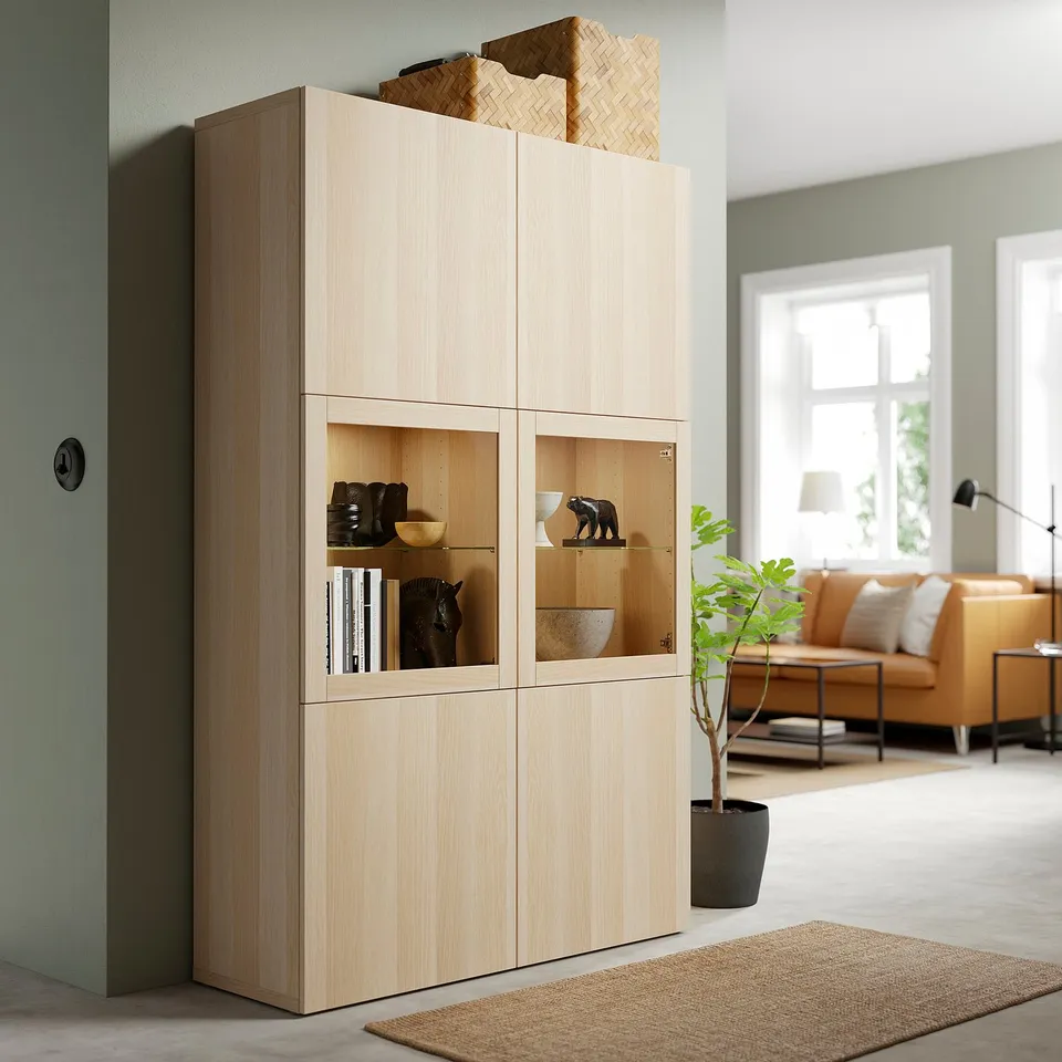 Oak BESTÅ storage with glass doors near window, displaying decor.