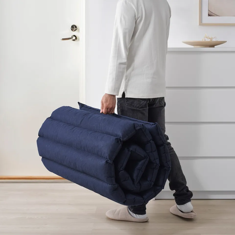 Person carrying rolled-up blue futon mattress, showing ease of transport and storage.