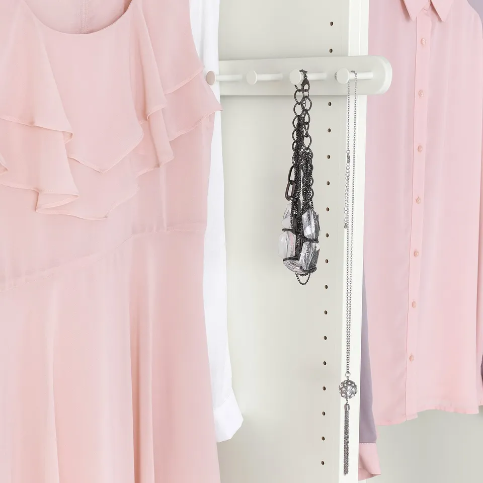White closet organiser hanging two necklaces and a bracelet between pink blouses.