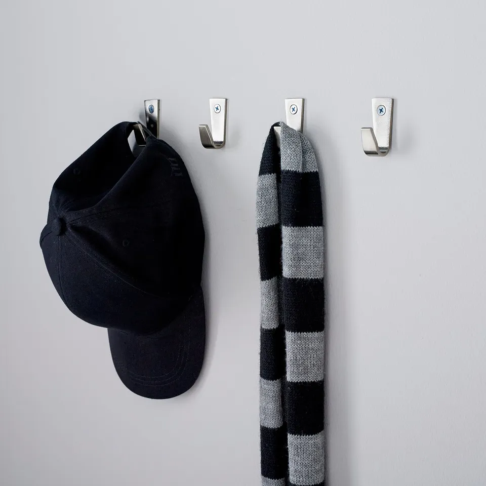 Four metallic wall hooks hold a black cap and a striped scarf, neatly organising accessories in a hallway.