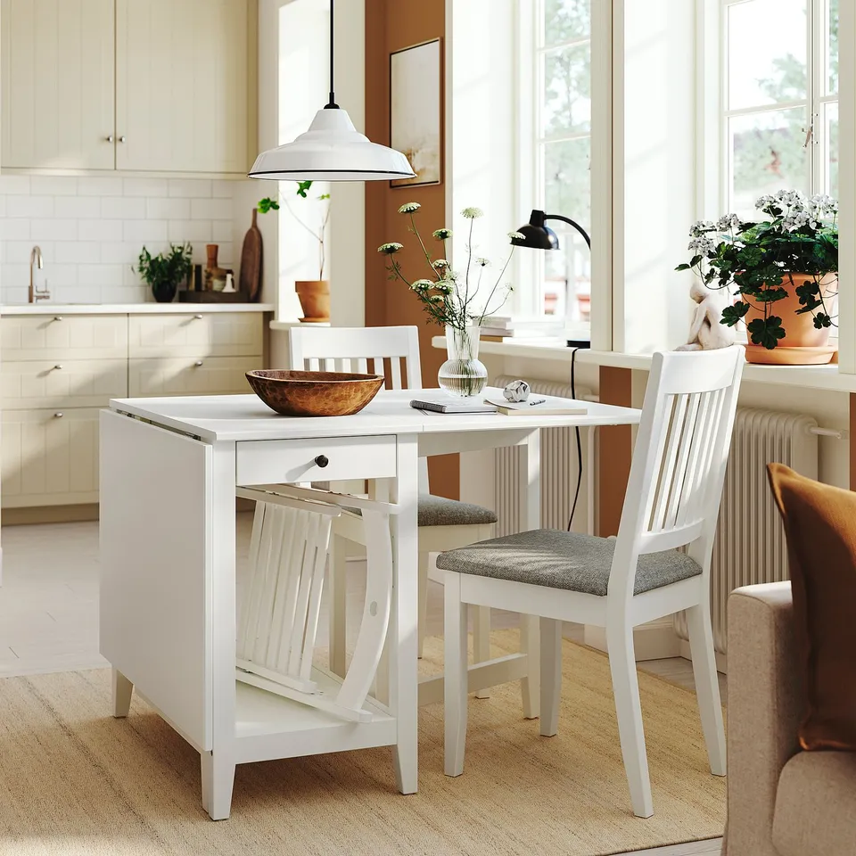 White gateleg table with chairs, flowers, storage, lamp, window.