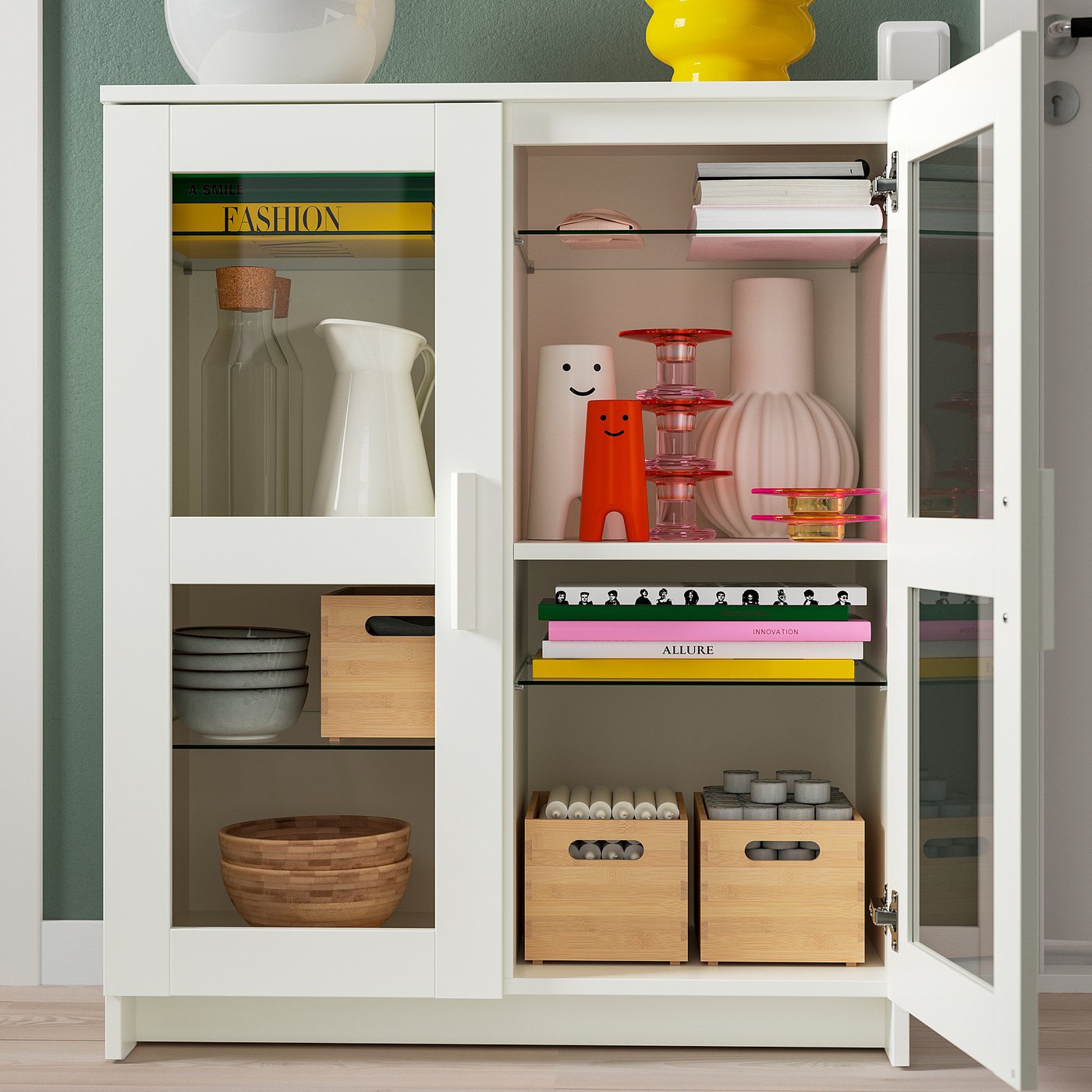 White cabinet with glass doors showcasing vases, bowls, books, and boxes. Shelves are adjustable and the cabinet is fixed to the wall.