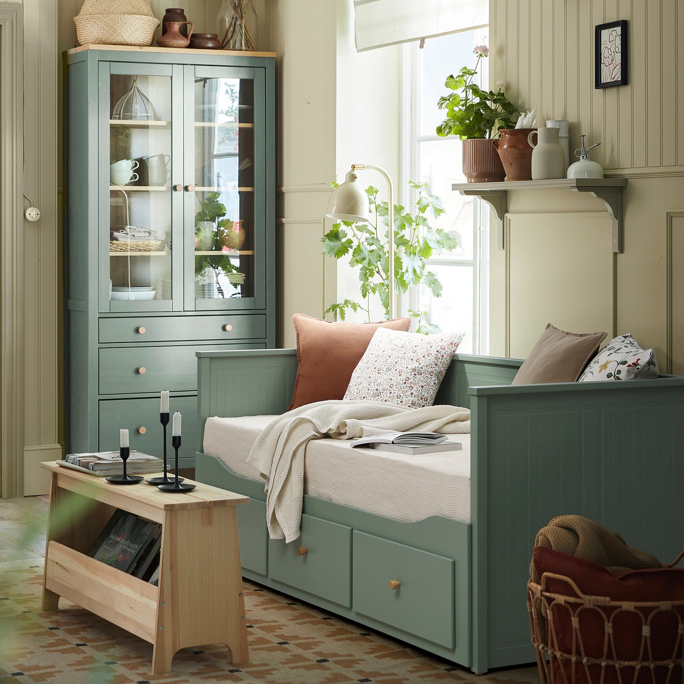 HEMNES day-bed in grey-green, styled as sofa, by window next to cabinets & cosy nook with blanket and books.