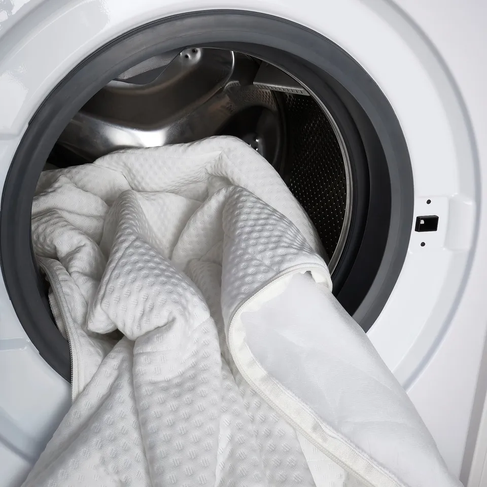 White washing machine filled with large white comforter, showing drums capacity and laundry functionality.